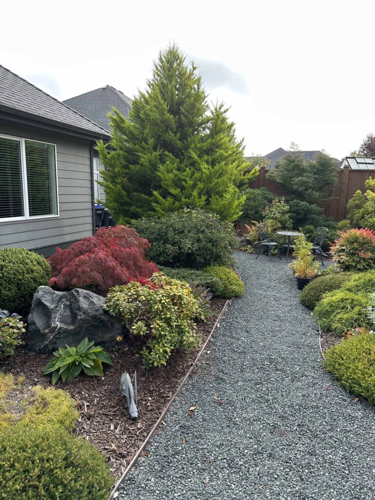 IMG_1391-scaled Landscaping example: A table and two chairs on a pebbled path, surrounded by a colourful landscape.